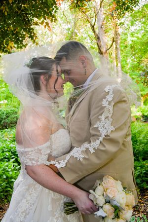 A romantic wedding couple embraces in a lush garden setting with soft natural lighting and delicate lace details.