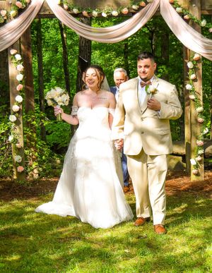 A couple celebrates their wedding day with joyful dance moves under elegant white drapes and floral decorations outdoors.