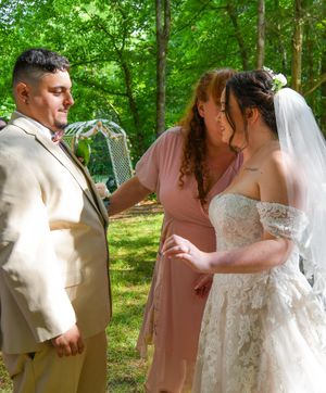 A couple shares a romantic first look moment in a lush green forest setting wearing wedding attire.