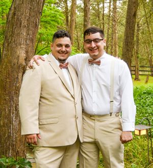 Two people in formal attire with bow ties pose together against a wooded backdrop.