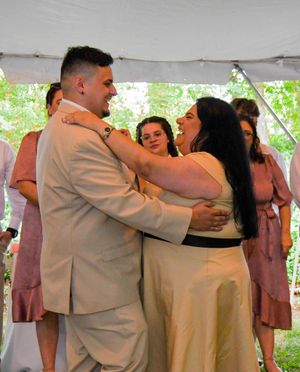 A couple shares their first dance at an outdoor wedding reception under a white tent with guests watching.
