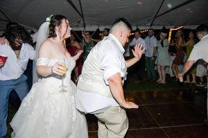 People dancing and celebrating at a wedding reception under a tent with dim lighting and festive atmosphere.