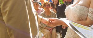 Close-up of hands exchanging rings during an outdoor wedding ceremony with guests seated in background.