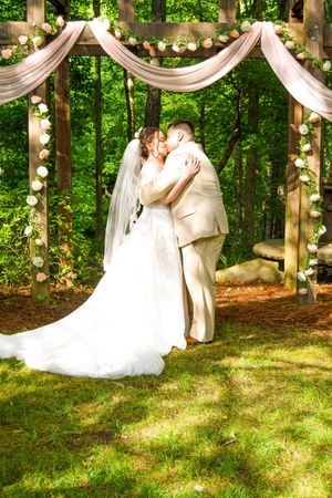 A romantic outdoor wedding ceremony in a wooded setting with white drapes and string lights creating an enchanting atmosphere.