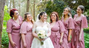 Wedding party wearing dusty rose bridesmaid dresses poses together in a lush garden setting.