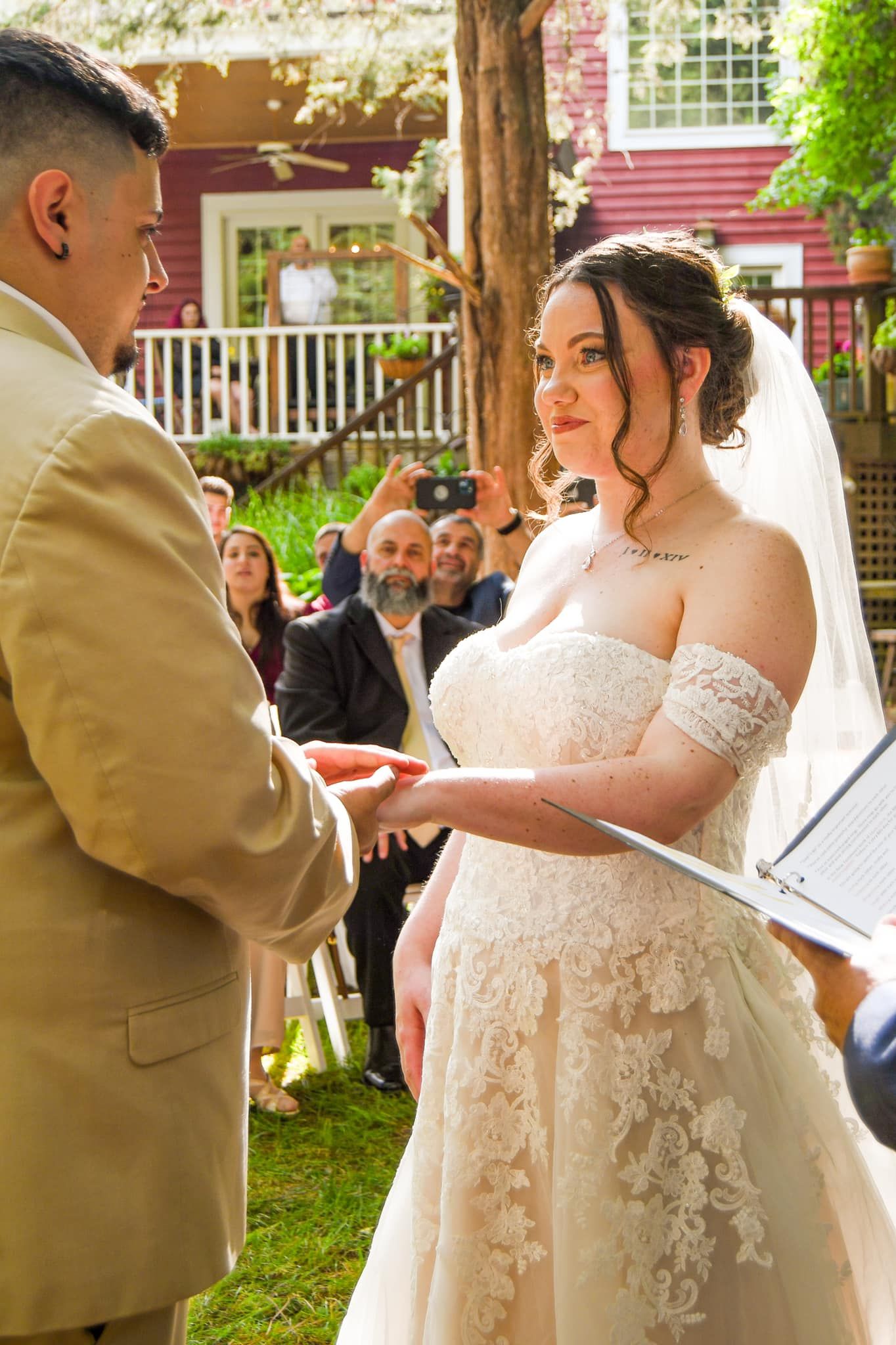 A couple exchanges vows during an outdoor garden wedding ceremony with guests watching in the background.