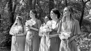 Wedding party members in light blue dresses and white bouquets stand together outdoors in a garden setting.