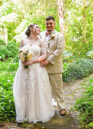A couple shares a romantic moment on a garden path surrounded by lush greenery during their wedding photoshoot.