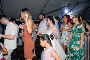 Wedding guests dance and celebrate on a dimly lit dance floor under a tent.