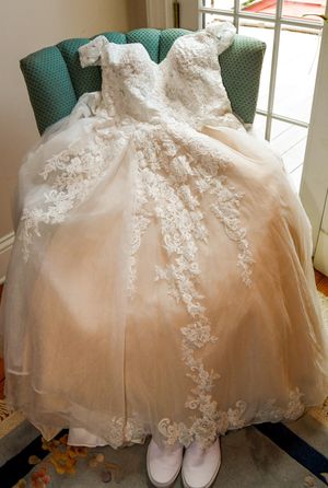 A delicate white christening gown with lace details and embellishments displayed on a green chair.