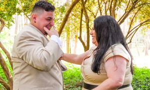 A couple shares a joyful moment together outdoors with sunlit trees in the background.