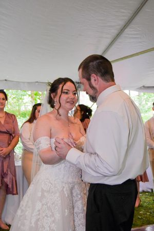 Newlyweds share their first dance under a white tent at an outdoor wedding reception.