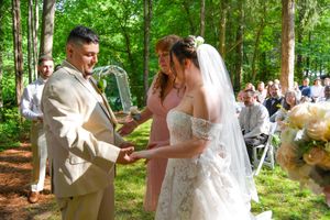 An outdoor forest wedding ceremony with a couple exchanging vows under an arch with white chairs.