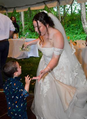 A young child in a patterned shirt dances with someone wearing a white wedding dress at a reception celebration.