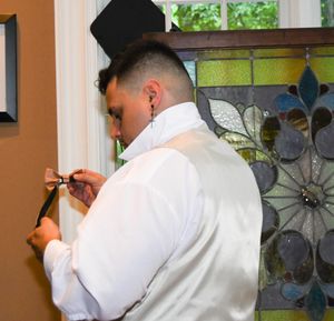 A person in a white dress shirt adjusts their collar while standing in front of a colorful window.