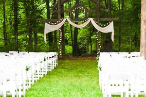 White chairs set up for an outdoor forest wedding ceremony with draped fabric decorations.