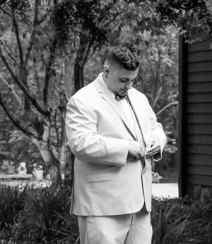A person wearing a white formal outfit stands in a black and white photograph.