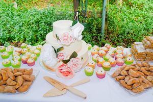 A dessert table with colorful cupcakes, cookies and a tiered cake decorated with pink roses for a special occasion.