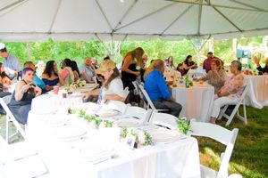 Wedding guests seated at elegantly decorated tables under a white outdoor tent during a daytime reception celebration.