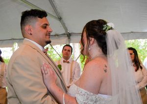 Wedding couple shares an intimate moment during their first dance under a white tent at an outdoor reception.