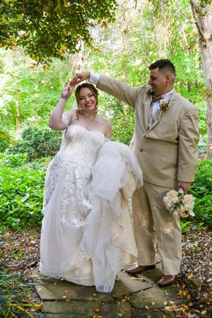 A wedding couple shares joyful moments in a lush garden setting, with the bride wearing a white dress and groom in tan suit.