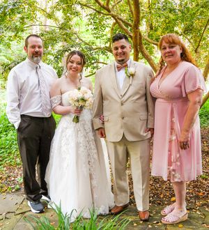 Wedding party in pink and beige attire poses together in a lush garden setting during summer celebration.
