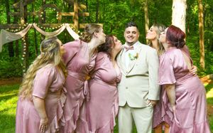 Wedding party in dusty rose bridesmaid dresses poses for photos in a lush green outdoor setting.