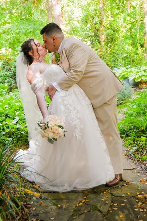 Wedding couple shares romantic kisses in a sunlit forest pathway.