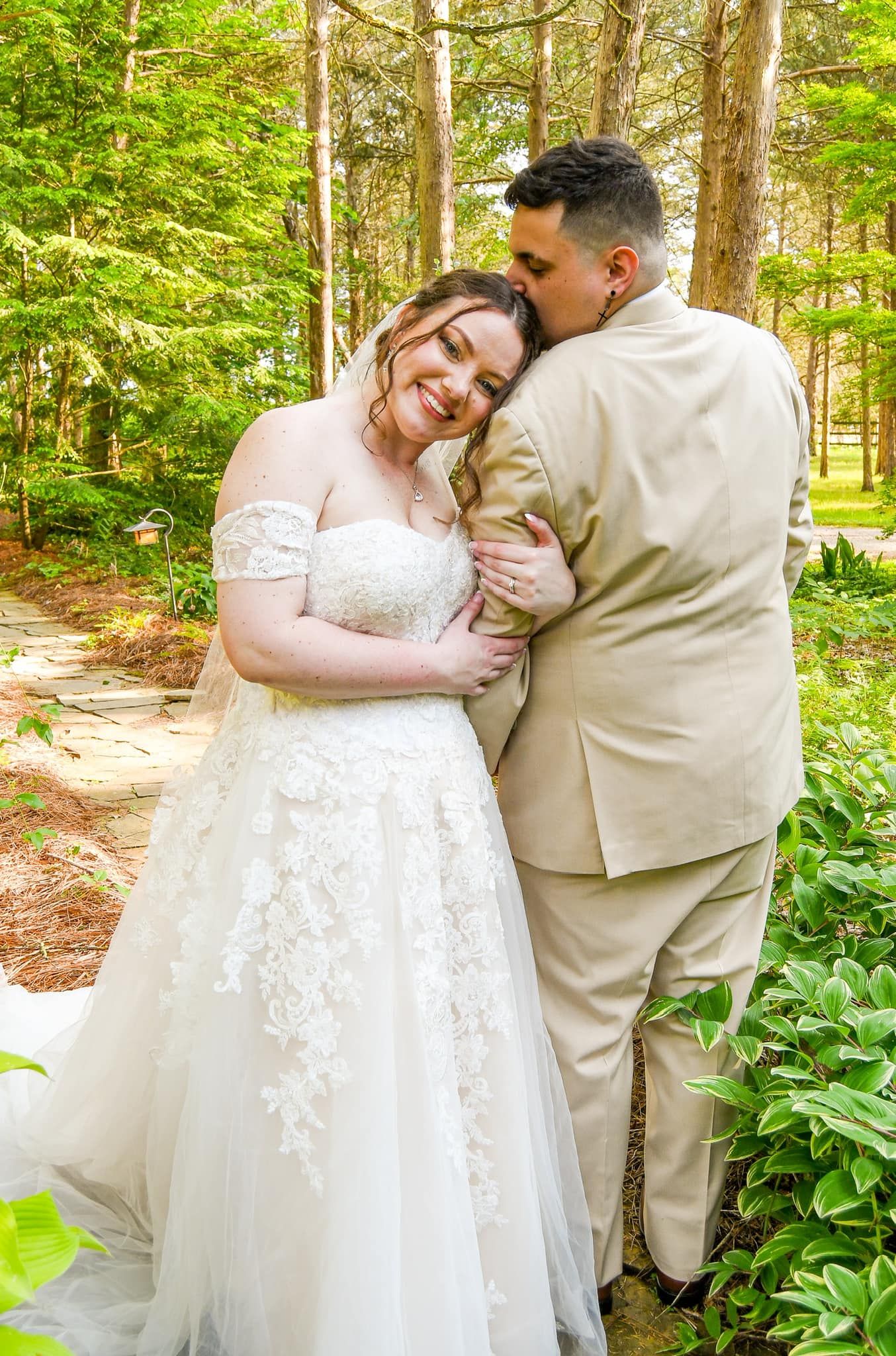 Newlyweds embrace tenderly in a wooded outdoor setting with natural greenery.