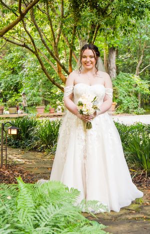 Wedding party in white dresses poses along garden pathway with lush ferns.