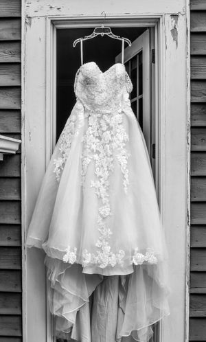 White lace wedding dress with floral details hangs elegantly against rustic wooden siding.