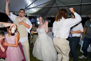 People dancing and celebrating at a wedding reception under a white tent canopy.