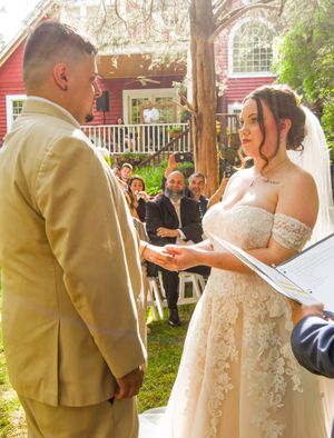 A couple exchanges rings during an outdoor garden wedding ceremony while guests look on from white chairs.