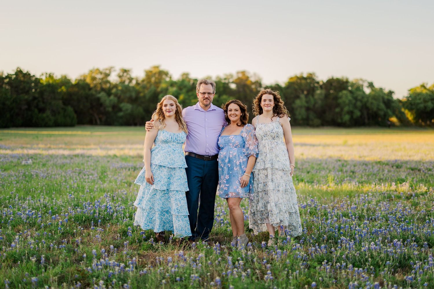 Family posing together in bluebonnet field for a spring mini session in Central Texas with vibrant wildflower backdrop.