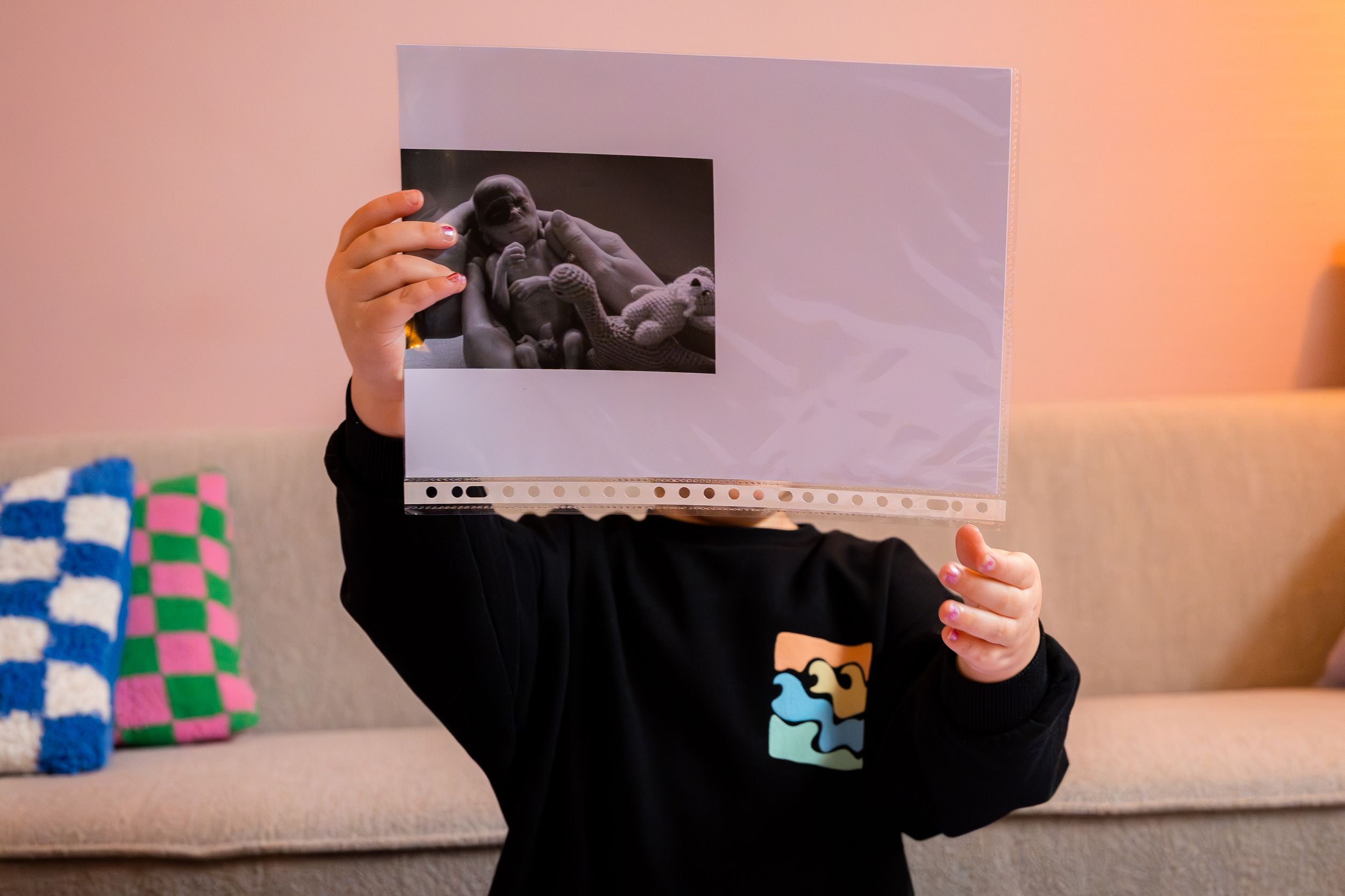 Someone holds up a series of black and white photographs in a dimly lit room with orange ambient lighting.