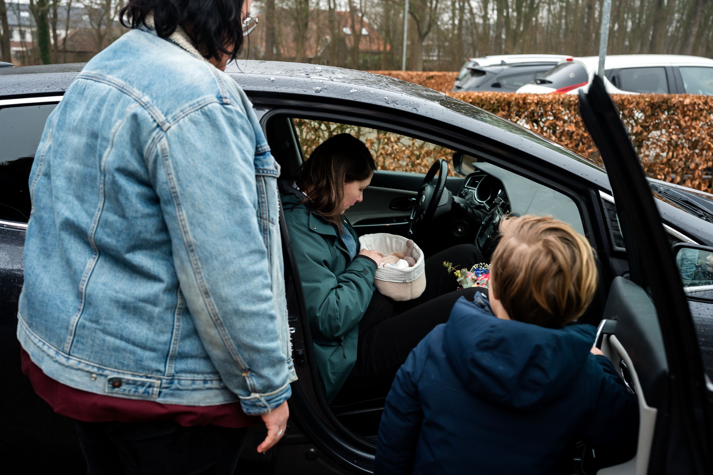 A person in a denim jacket gets into a car while holding a coffee cup in their hand.