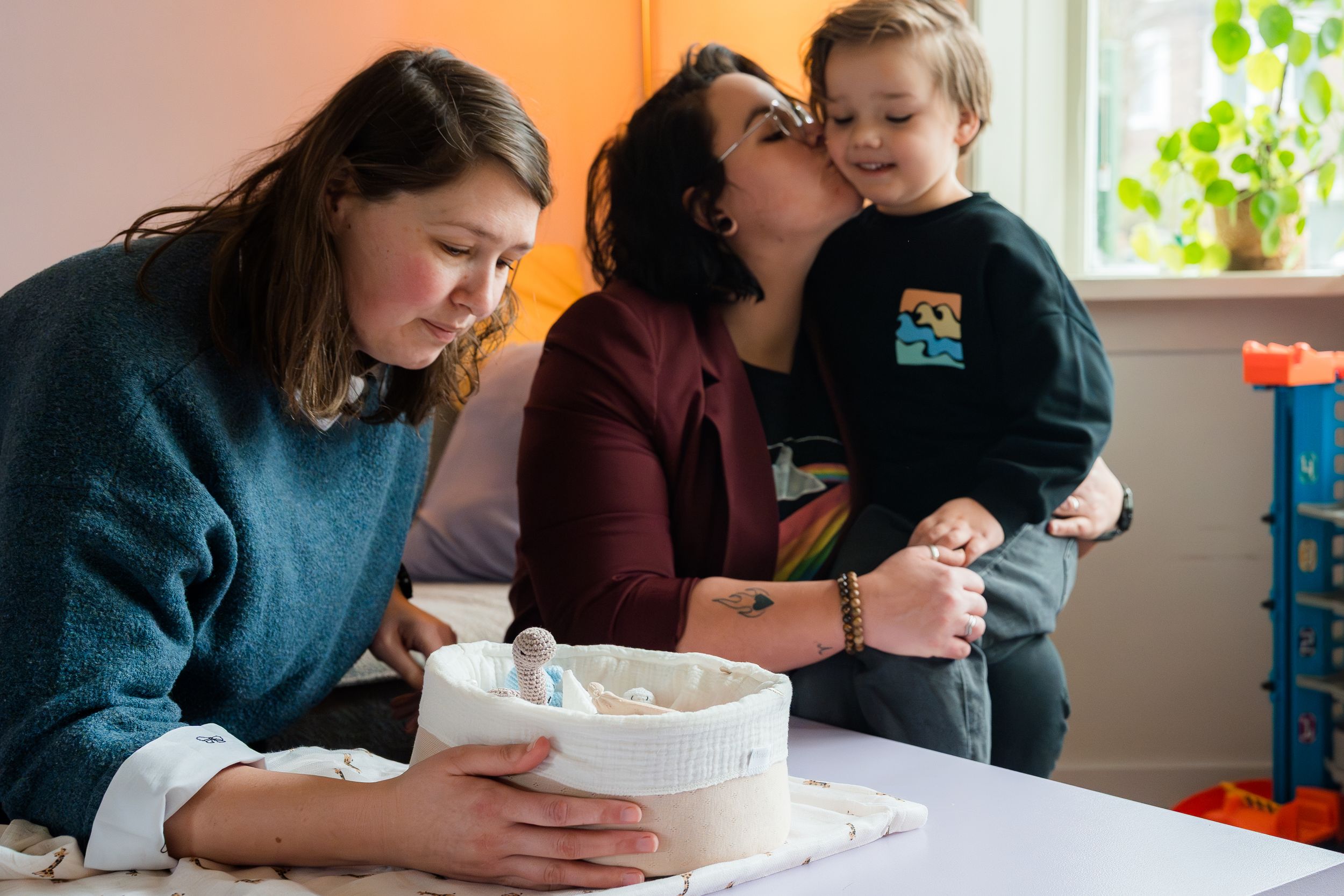 A cozy family moment in a bright room as someone decorates a cake while others share an affectionate moment nearby.