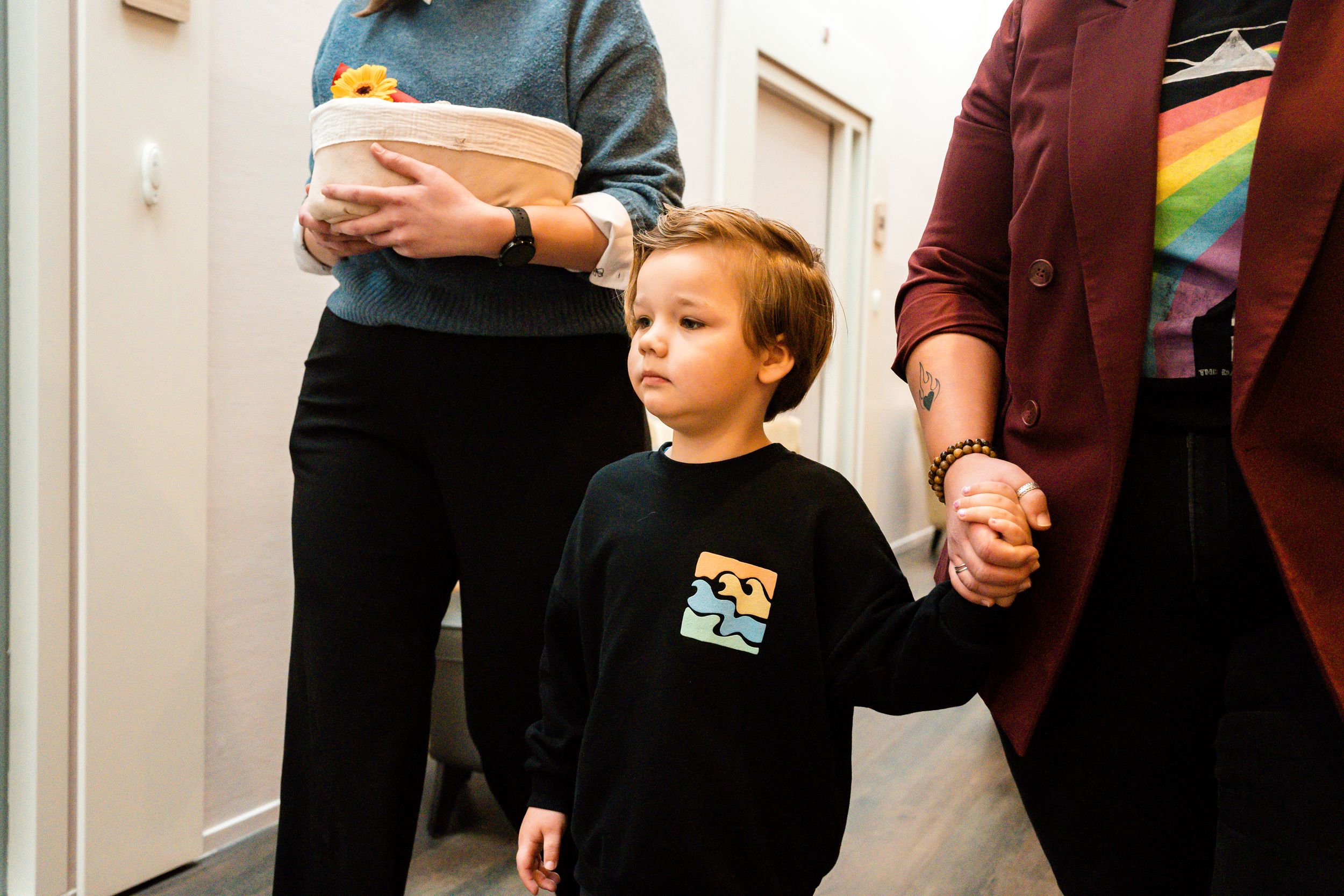 A person holds a young child's hand while walking through a hallway with other people.