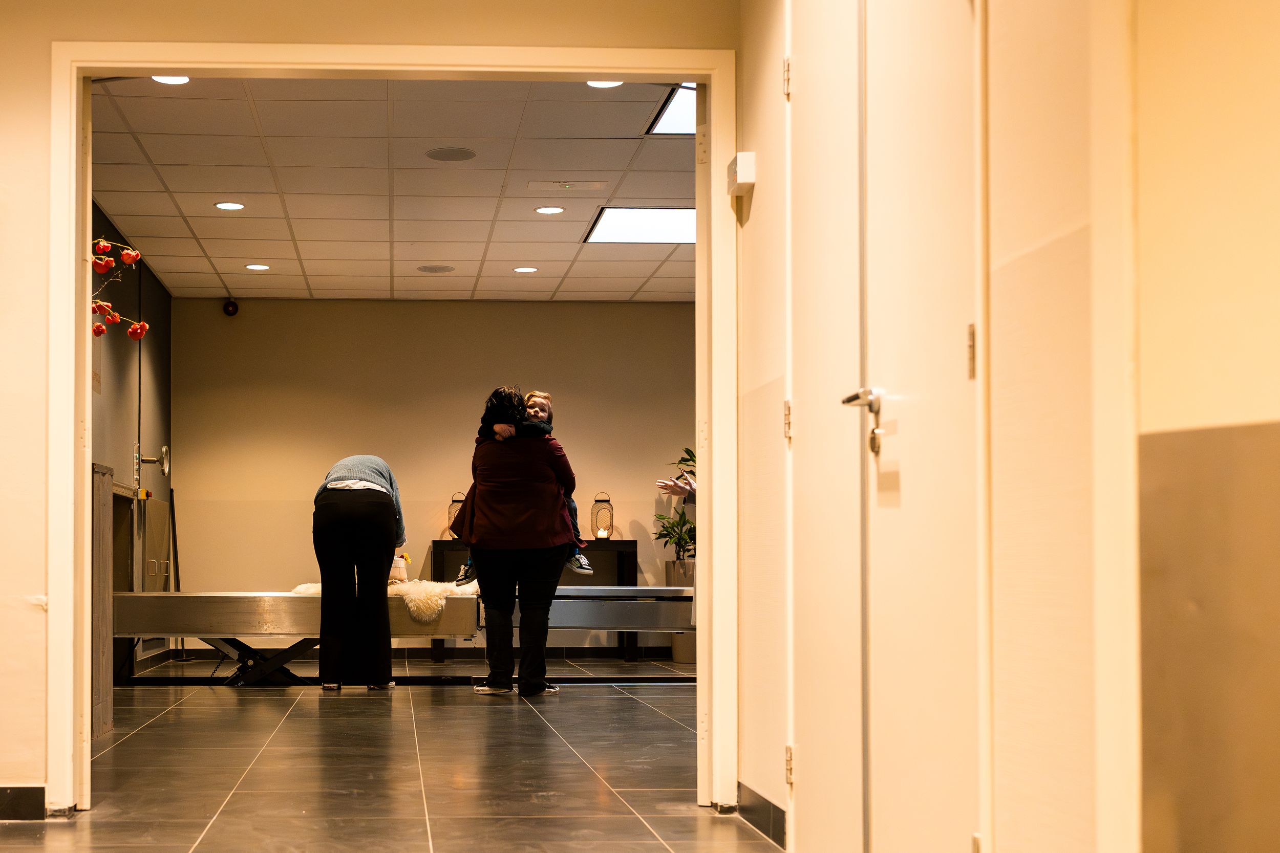 Long beige hallway with fluorescent lighting and dark trim along the walls leading to a distant doorway.