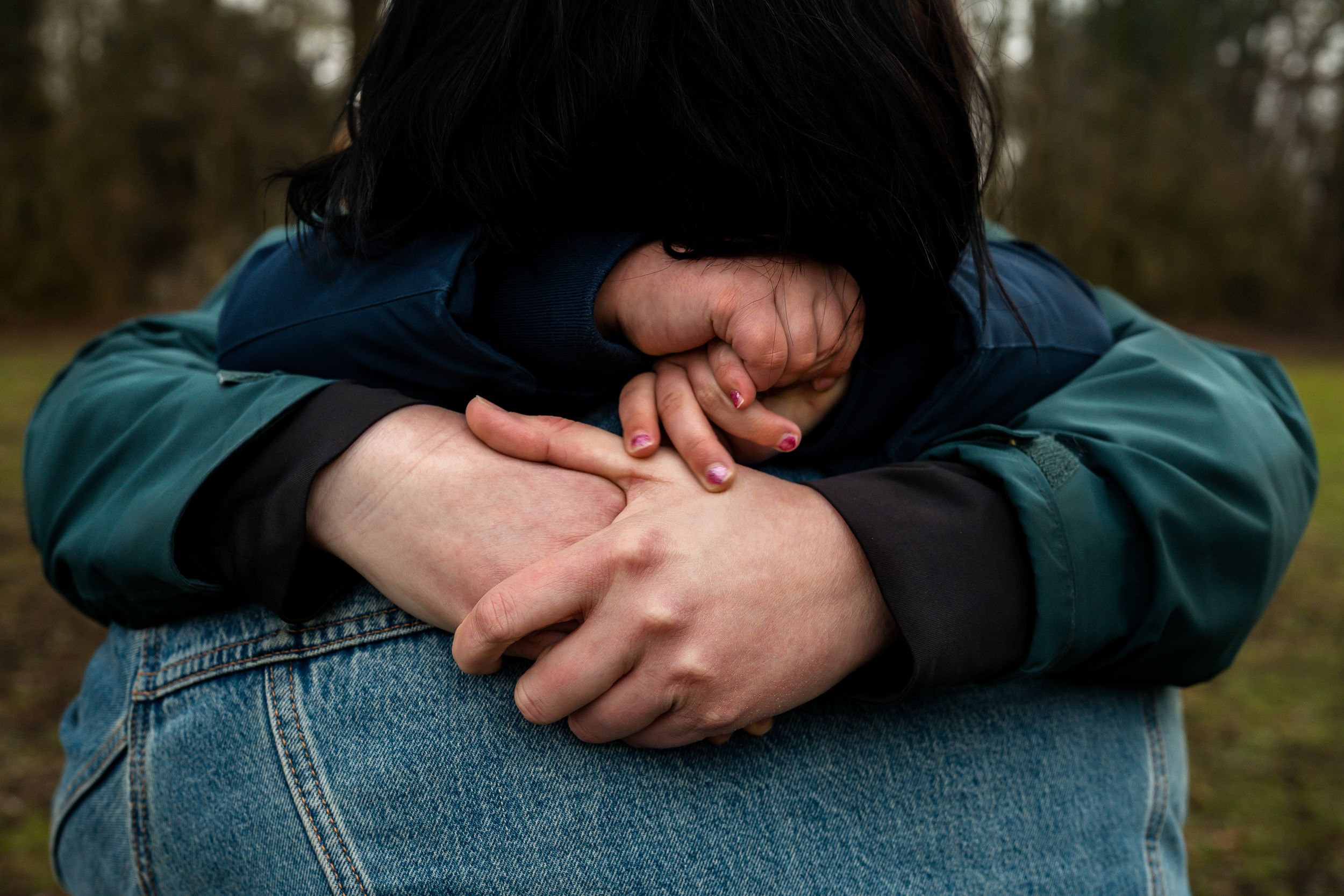 Close-up photo of hands wearing denim jeans and a teal jacket against a blurred outdoor background.
