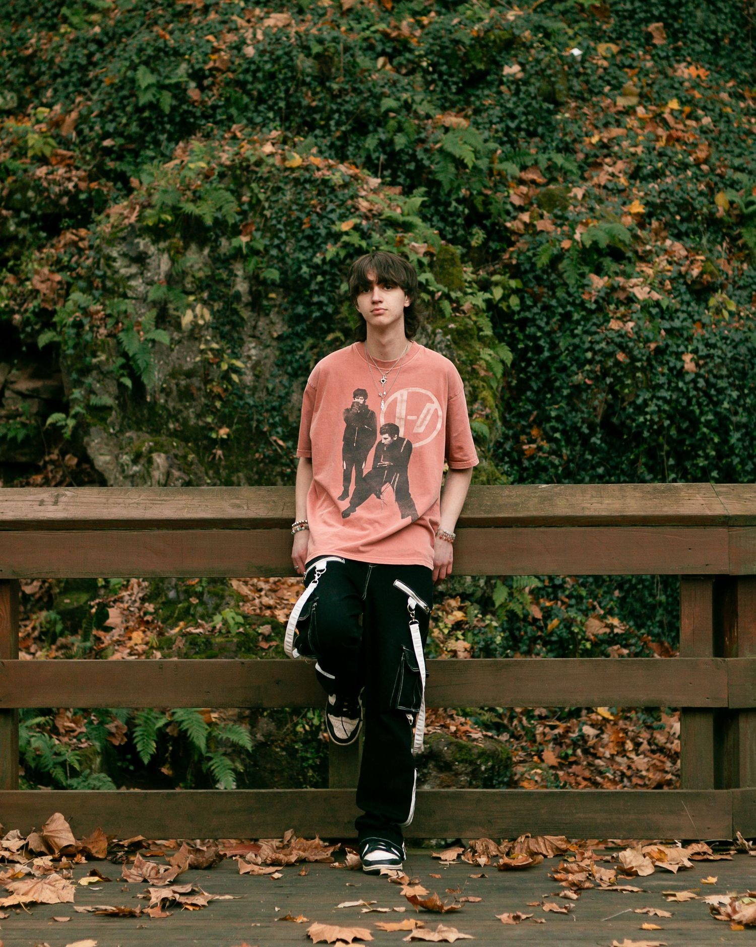 Someone sits on a wooden bench surrounded by fallen autumn leaves and green foliage in the background.