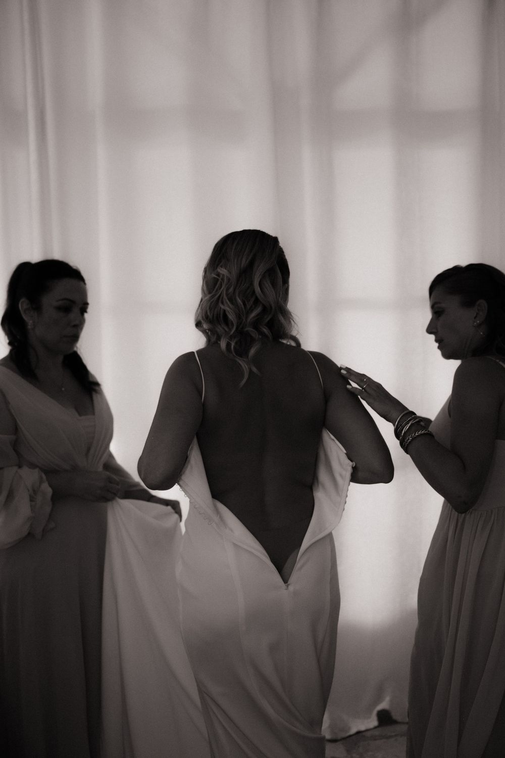 Silhouette d'une mariée de dos qui enfile sa robe à l'aide de ses témoins.