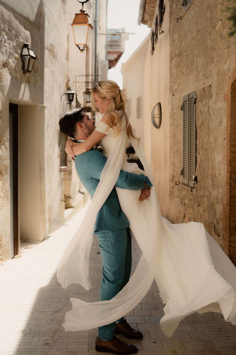 Mariage dans les ruelles de Mougins - Les jeunes mariés célèbrent ce moment en dansant, le marié porte sa femme et tourne et sa robe vole .