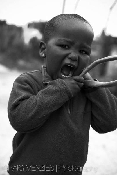 Young African child biting a stick with mouth wide open in black and white photo.