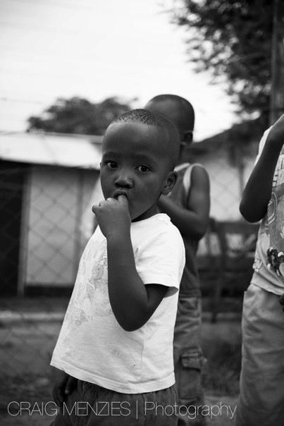 Small African child in white t-shirt with hand near mouth in black and white photo.