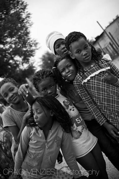 Group of African children and a woman posing together outdoors in black and white photo.