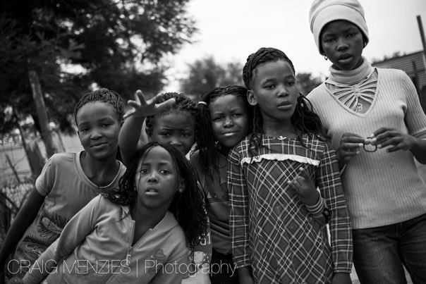 Group of African girls and a woman posing together on a street in black and white.