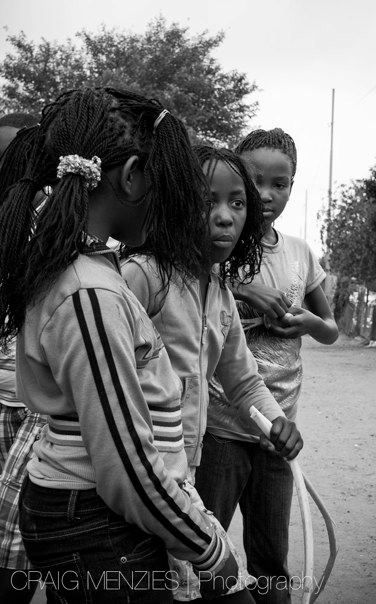Three African girls with braided hair standing together outdoors in black and white photo.