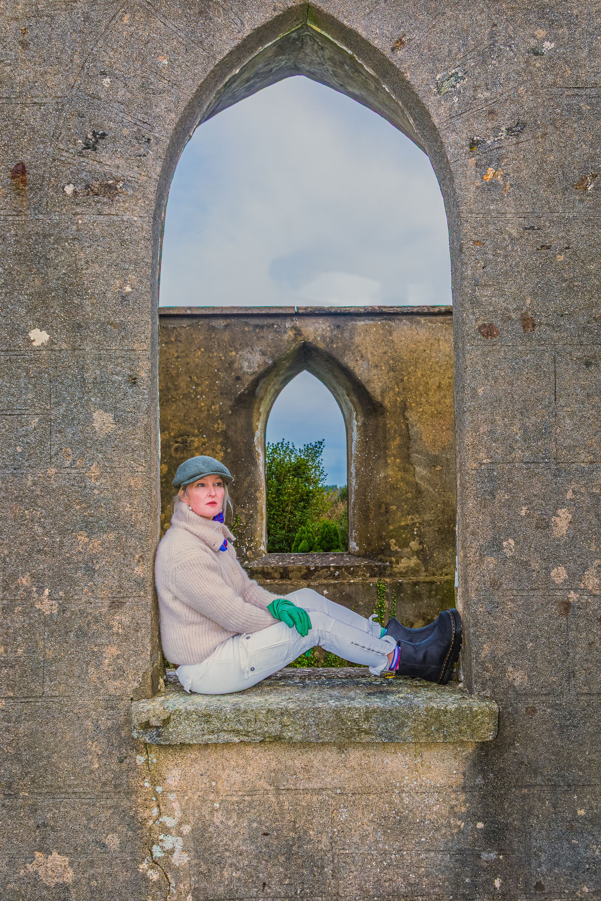 Three arched stone alcoves in an old church wall with a woman sitting and relaxing in a stoney windowsil.
