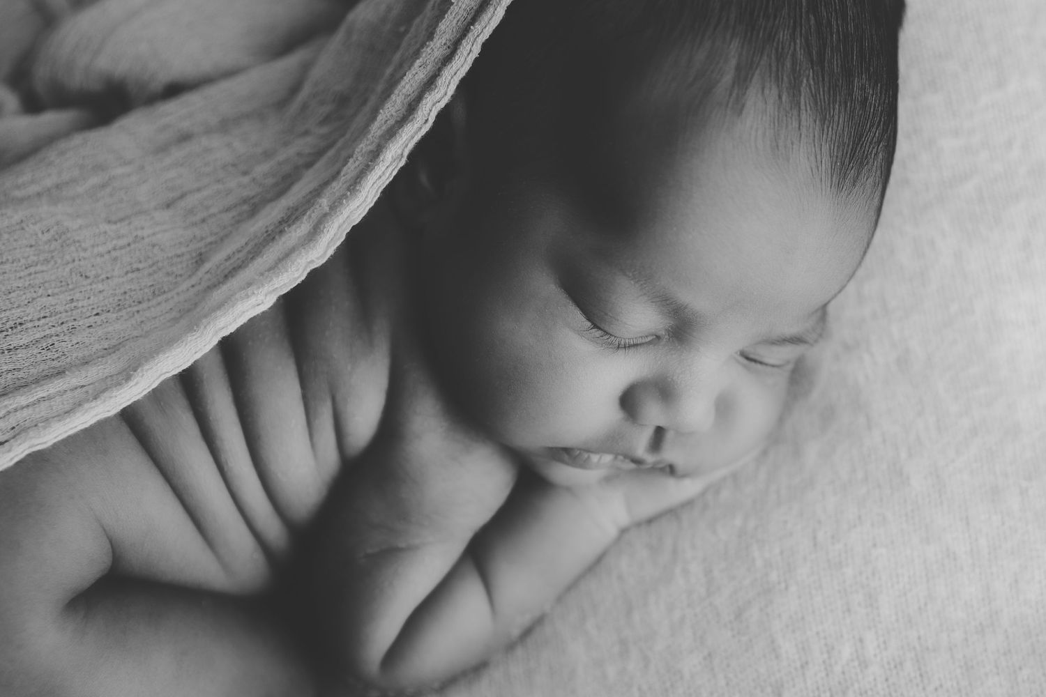 Newborn baby sleeping peacefully on soft beige blanket wearing delicate floral headband in natural light.